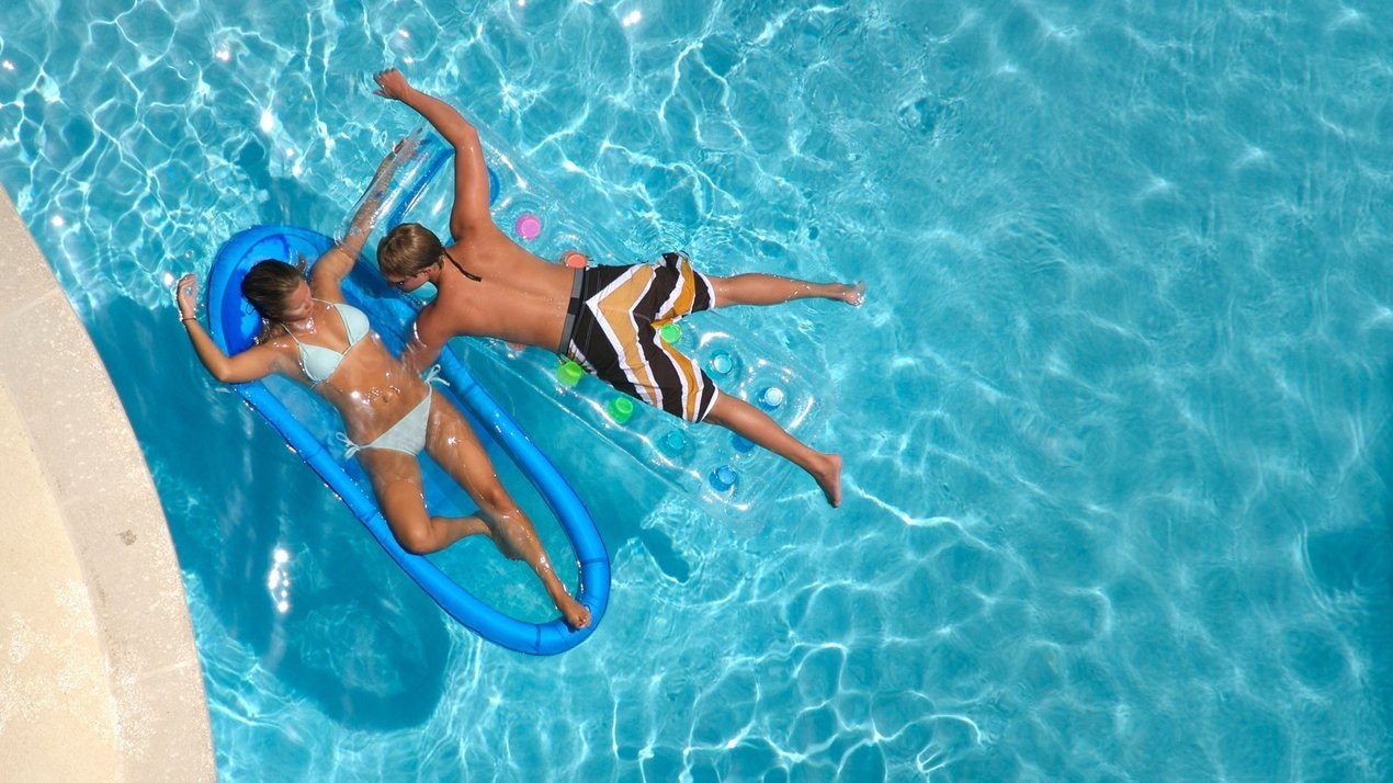 Top-Down-Ansicht eines Paares auf aufblasbaren Luftmatratzen in einem Swimmingpool
